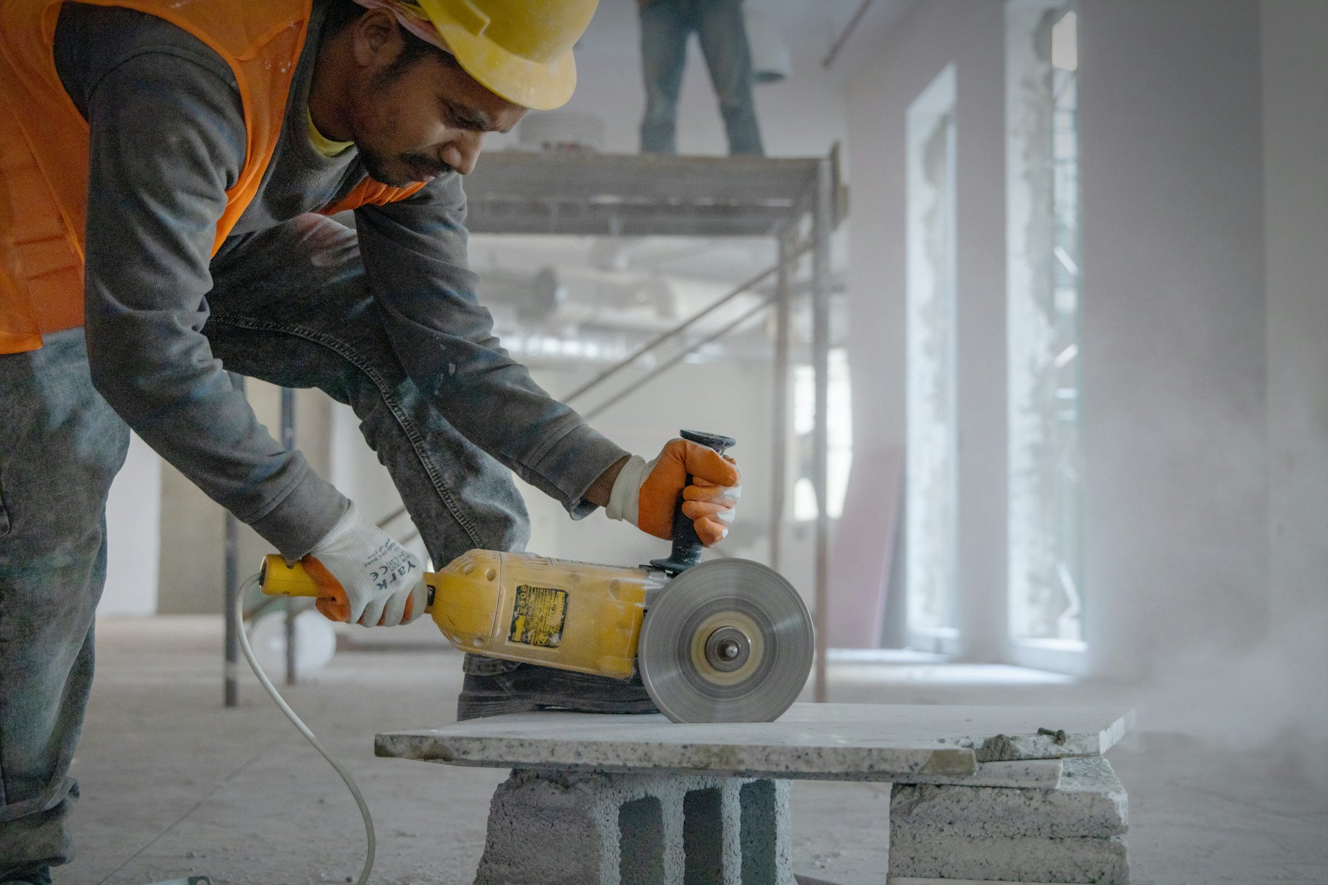 Operator in orange hi-vis cutting a concrete slab with a cut-off saw, dust rising